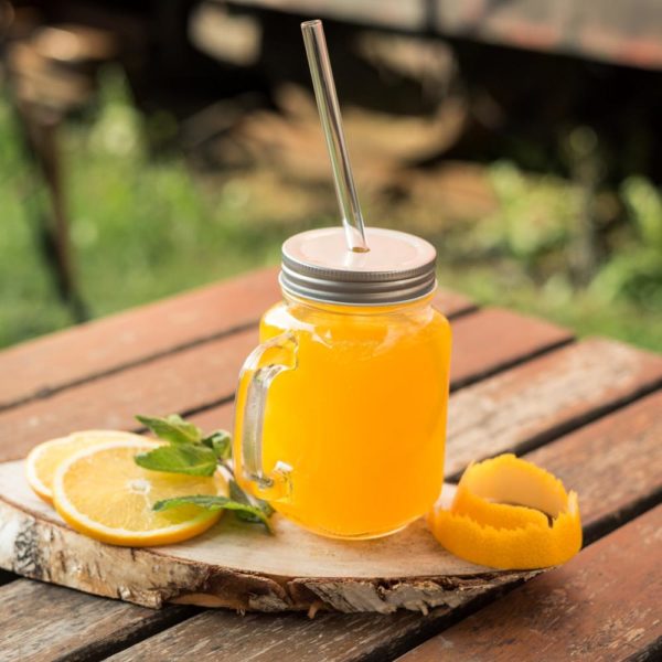 Wiederverwendbarer Trinkhalm aus Glas in Trinkglas auf Tisch serviert mit Orangen
